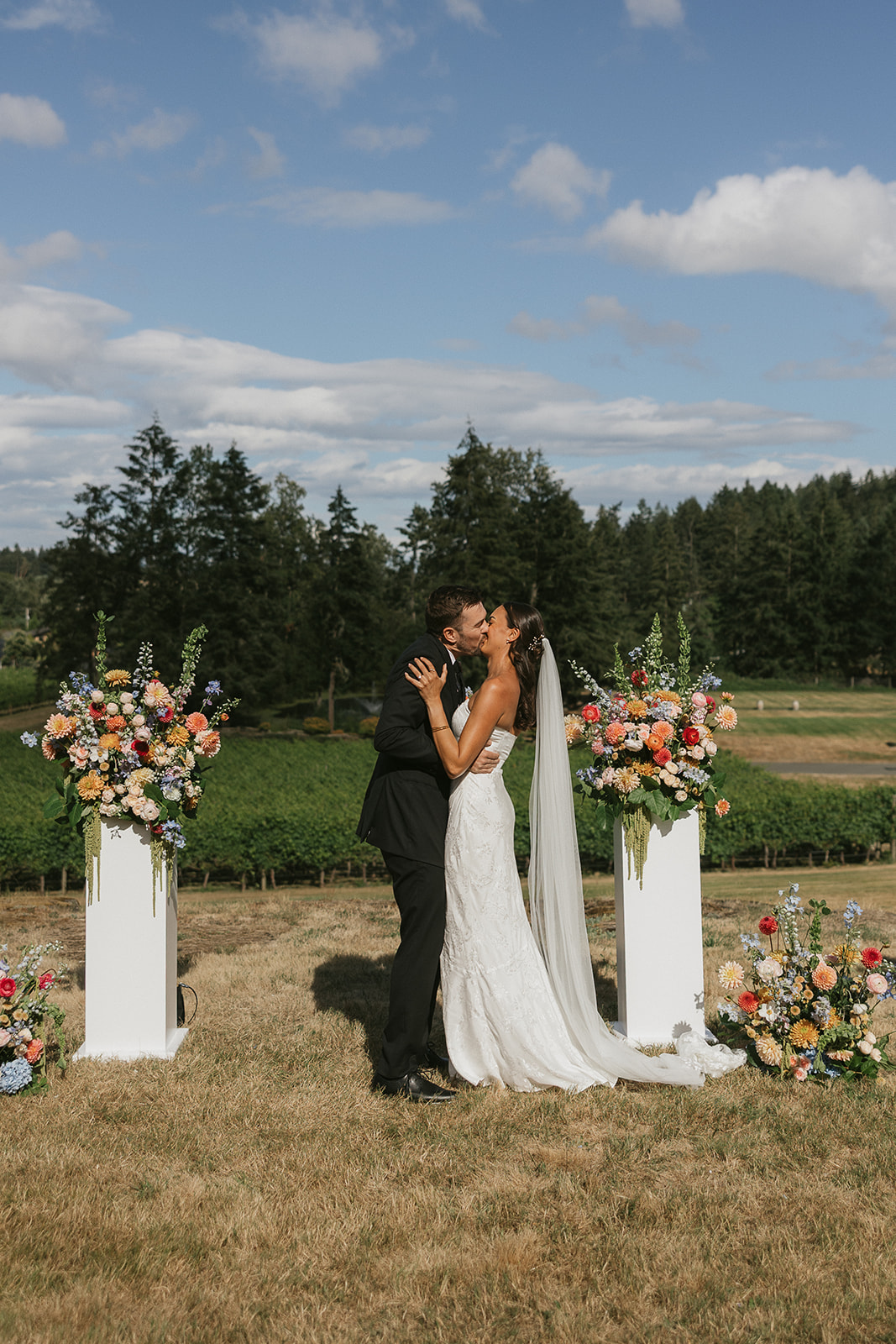 Bride and groom kissing at a floral-flanked wedding ceremony arch in Victoria, BC